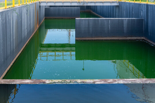 Industrial wastewater treatment or sedimentation tanks filled with green water divided by steel partitions at an industrial facility showing environmental water management infrastructure.