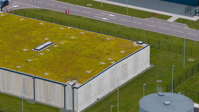Aerial view of a modern industrial building with a green sedum roof, concrete walls, and surrounding infrastructure including a circular tank in Middenmeer, North Holland, Netherlands.