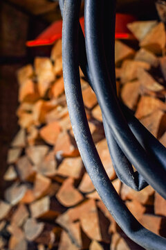 Black rubber garden hose hanging in loops inside a rustic shed with stacked firewood