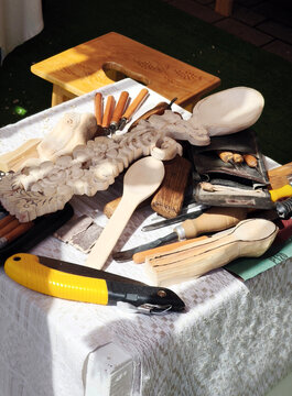 Woodcarving workspace with tools and unfinished wooden pieces. Carving knives, chisels, spoons, and reliefs highlight artisan process and craftsmanship in progress