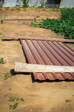 Brown corrugated metal sheet resting on sandy soil in a rural garden