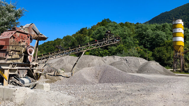 Heavy quarry crushing plant with long conveyor belts sorting and piling aggregate and gravel in an open pit industrial site under a clear blue sky
