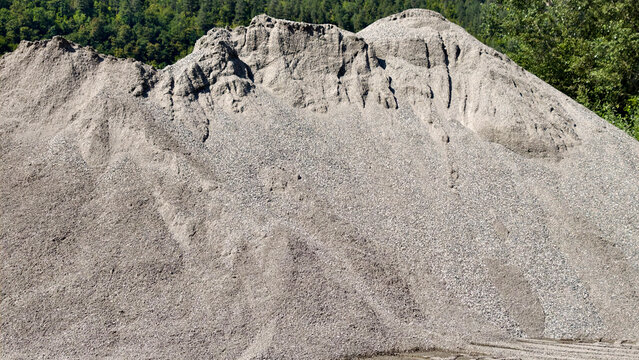 Large gravel and sand piles forming hills with a forest background, representing construction materials, industry, excavation, and building resources