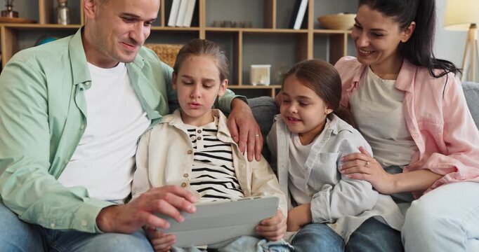 Family parents daughters with tablet at home. On a cozy couch they browse, learn, and watching together, sharing smiles in a bright living room. Message is family bonding through technology.