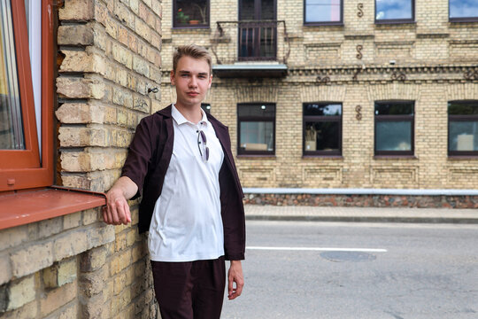blonde man in brown clothing standing on a European city street with classic architecture urban lifestyle atmosphere.