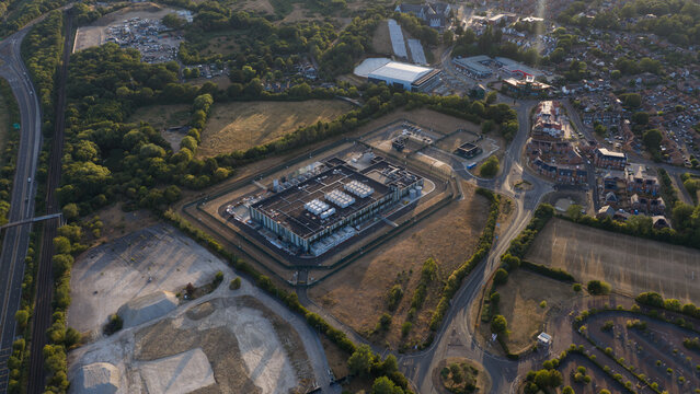 Aerial view of a data center facility surrounded by perimeter fencing, adjacent to a highway and suburban residential area in Bracknell, England, United Kingdom.