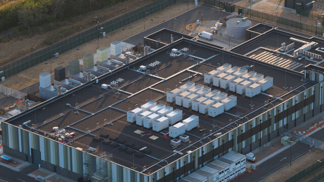 Aerial view of a modern data center facility featuring numerous HVAC cooling units on the flat roof, surrounded by security fencing in Bracknell, England, United Kingdom.