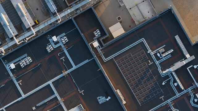 Aerial view of a flat industrial building roof featuring solar panels, HVAC units, and ventilation pipes in Bracknell, England, United Kingdom.