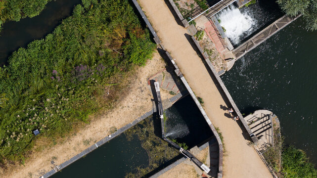 Aerial view of Fobney Pumping Station lock system with a bridge, lush green vegetation, and people walking along the path in Reading, England, United Kingdom.
