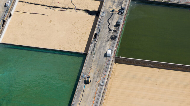 Aerial view of rectangular water treatment basins with sand and water, featuring concrete walkways and industrial equipment in Reading, England, United Kingdom.