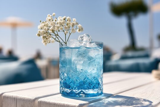 Refreshing blue cocktail with ice and delicate white flowers at a sunny beach resort