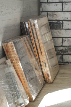Disassembled wooden furniture panels wrapped in transparent stretch film indoors, illustrating moving preparation, furniture storage, transportation and renovation