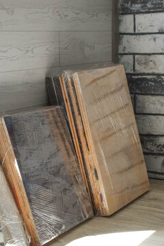 Disassembled wooden furniture panels wrapped in transparent stretch film indoors, illustrating moving preparation, furniture storage, transportation and renovation