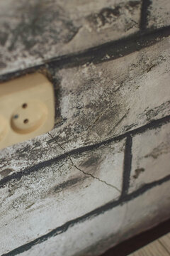 Close-up of an old beige electrical outlet on distressed faux brick wallpaper, illustrating outdated home wiring, electrical repair and budget renovation