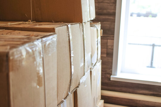 Stacked cardboard boxes sealed with packing tape near a window, illustrating moving, packing, storage, transportation and relocation logistics