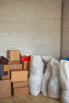 Stacked cardboard boxes and filled white woven bags indoors, illustrating moving preparation, household storage, packing and relocation
