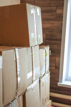 Tall stack of sealed cardboard moving boxes near a window, illustrating packing, relocation, household storage, transportation logistics and moving preparation