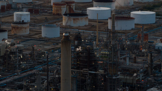 Aerial view of Fawley Refinery featuring industrial storage tanks, tall chimneys, and complex pipe networks under a dim evening sky in Southampton, England, United Kingdom.