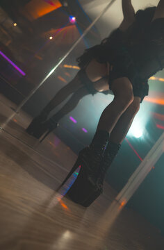 Pole dancer in high heels posing by a mirror with her reflection visible.