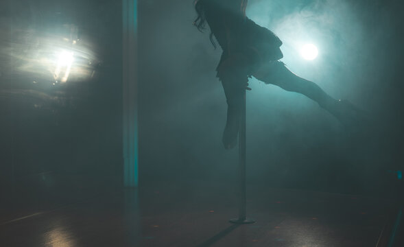 Pole dancer performing trick in smoky club.