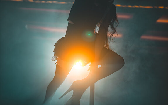 Pole dancer performing trick in smoky club.