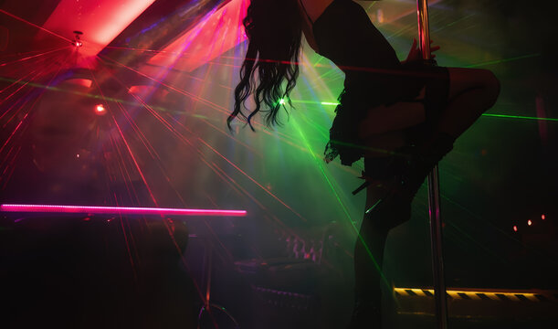 Pole dancer performing under laser lights in club.