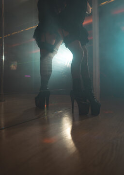 Pole dancer in high heels posing by a mirror with her reflection visible.