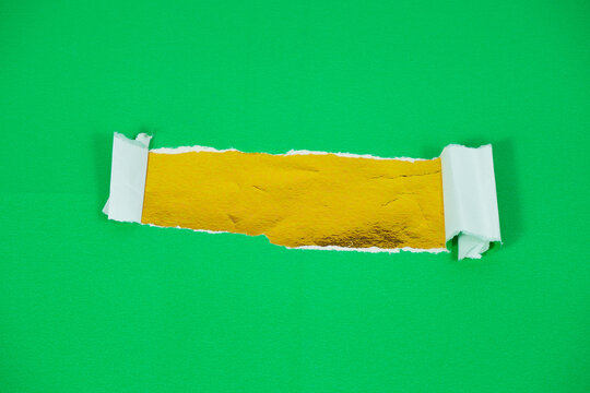 A gold foil layer behind torn green paper. Torn paper revealing a gold-backed area for text. The torn green paper layer peels back, exposing the gold foil layer underneath.
