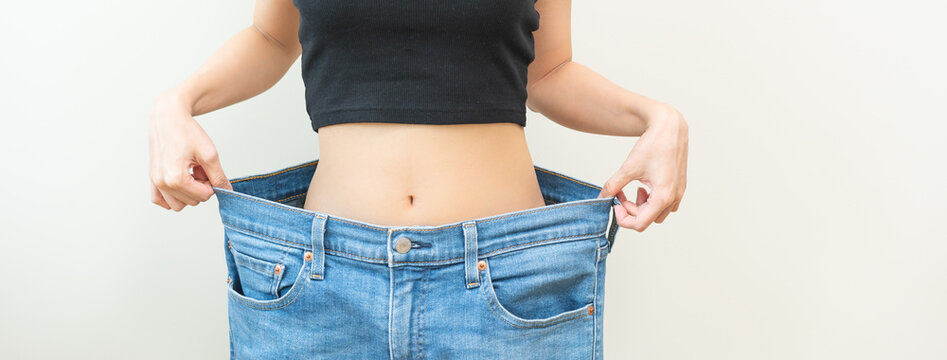 Shape slender, thin waist, slim fit asian young woman, showing body shape her weight loss, happy wearing in big, large or oversize jeans, excess lose by diet and exercise. Healthy lifestyle concept