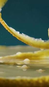 Vertical video: Falling citrus peel curls creating splashes on pale yellow viscous liquid in studio