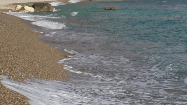 Beach wave pebble small white foamy waves gently rolling onto a brown pebble beach on a sunny day
