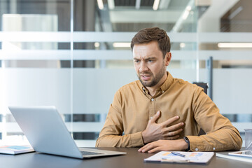 Obraz premium Businessman experiencing acute chest pain or heart attack while working at his office desk, indicating stress-related illness and medical emergency symptoms