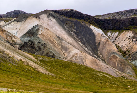 Aerial view of colorful volcanic mountains with rhyolite slopes and green grassy hills under a cloudy sky in Selfoss, Grimsnes- og Grafning, Iceland.