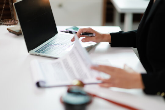 Legal professional working on laptop and reviewing documents, managing paperwork, offering consultation and justice representation at law firm office