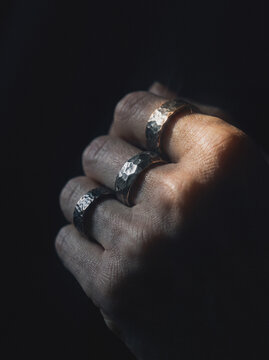 Hand wearing three hammered silver rings clenched in dramatic light, close-up jewelry detail