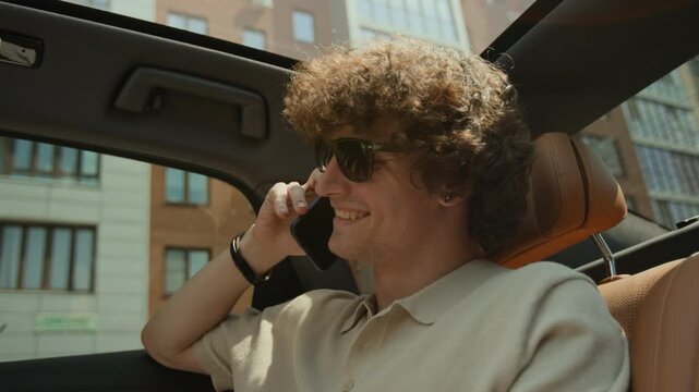Caucasian young adult man talking on smartphone while sitting in luxury car passenger seat. Perfect for mobile network advertisements or modern lifestyle promos