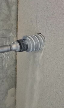 Vertical side close up video of a long shank core drill boring through a fair-faced concrete pylon for AC installation.
