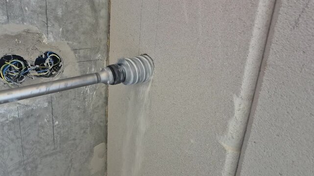 Side close up shot of a long shank core drill boring through a fair-faced concrete pylon for air conditioning pre-installation.