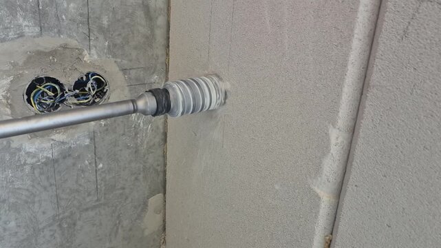 Slow motion side close up footage of a long shank core drill slowly boring through a fair-faced concrete pylon structure.