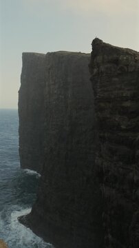 Majestic rocky cliffs plunging into the ocean on a misty day in Faroe Islands