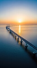Obraz premium An expansive aerial view of a long modern bridge stretching across the deep blue sea as the golden sun rises over the horizon at dawn, sunlight, serene, altitude