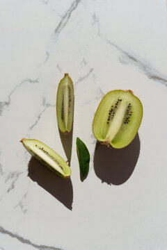 Vertical flat lay of fresh kiwi fruit slices and green leaf on marble.