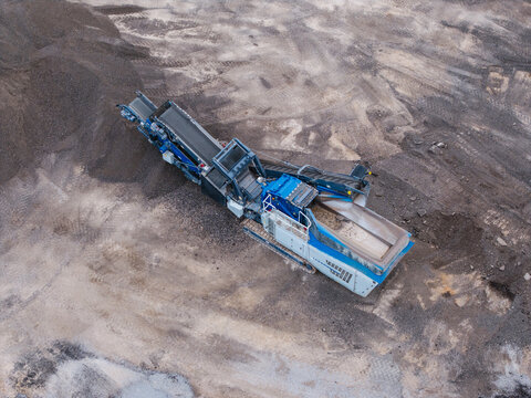 Aerial view of a mobile crushing and screening plant operating on a dirt site with piles of aggregate in Vecmokas, Tukums Municipality, Latvia.