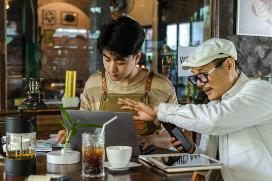 Modern family small business digital management, senior cafe owner guiding young barista worker or son sharing experience teamwork learning growth trust technology management lifestyle in coffee shop