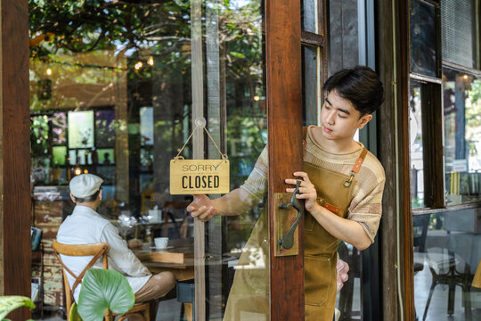 Yong small business owner opening cafe door with open sign displayed, inviting customers inside cozy coffee shop and restaurant, daily startup routine reflecting growth and opportunity in business.