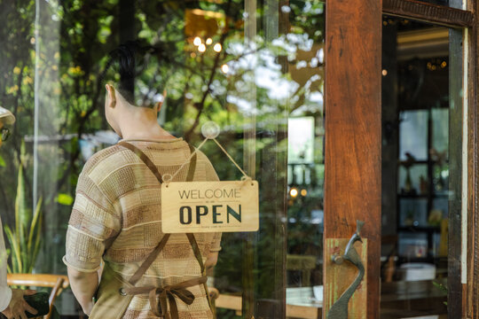 Young small business cafe owner placing closed sign on glass door, young entrepreneur ending daily service routine, reflecting on business operation and customer flow during quiet afternoon moment.
