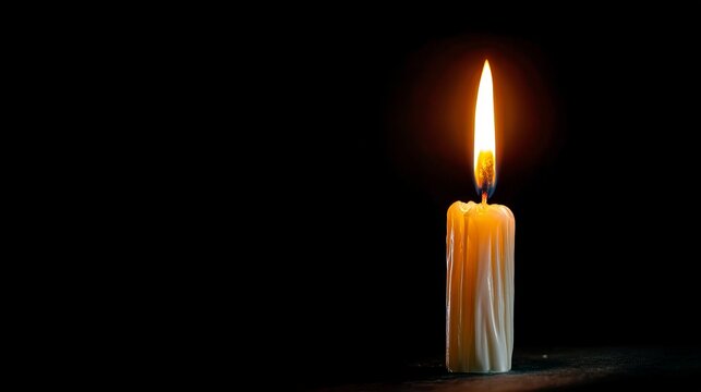 A single burning candle glows with warm orange flame in the dark fire light