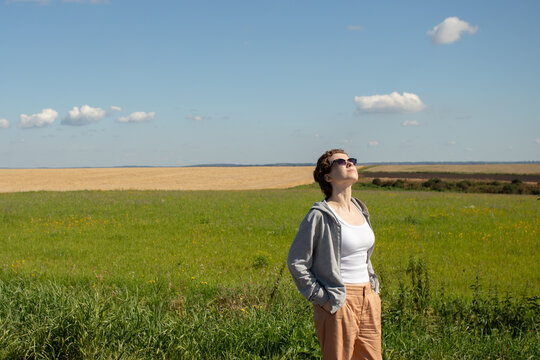 woman lifting her face toward the sunshine in an open green field, enjoying fresh air and a quiet nature break that supports relaxation, wellbeing and stress recovery