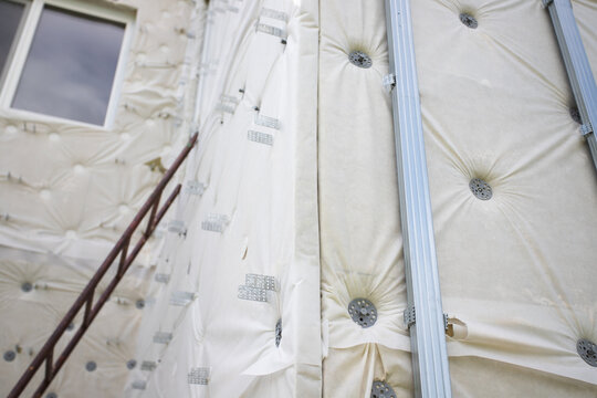low-angle view of a house under renovation with exterior insulation membrane, fasteners, metal battens and window, documenting energy retrofit before final cladding