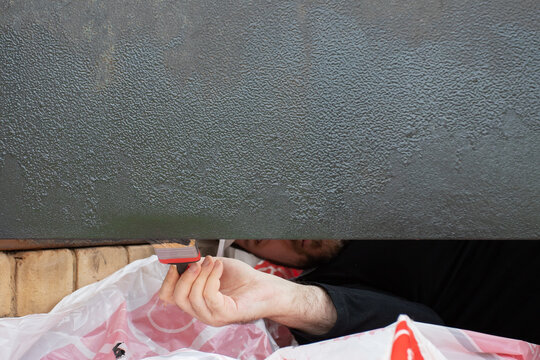 man reaching beneath an open steel entrance door to coat the lower edge with paint, treating a hard-to-reach area during corrosion repair and exterior home restoration
